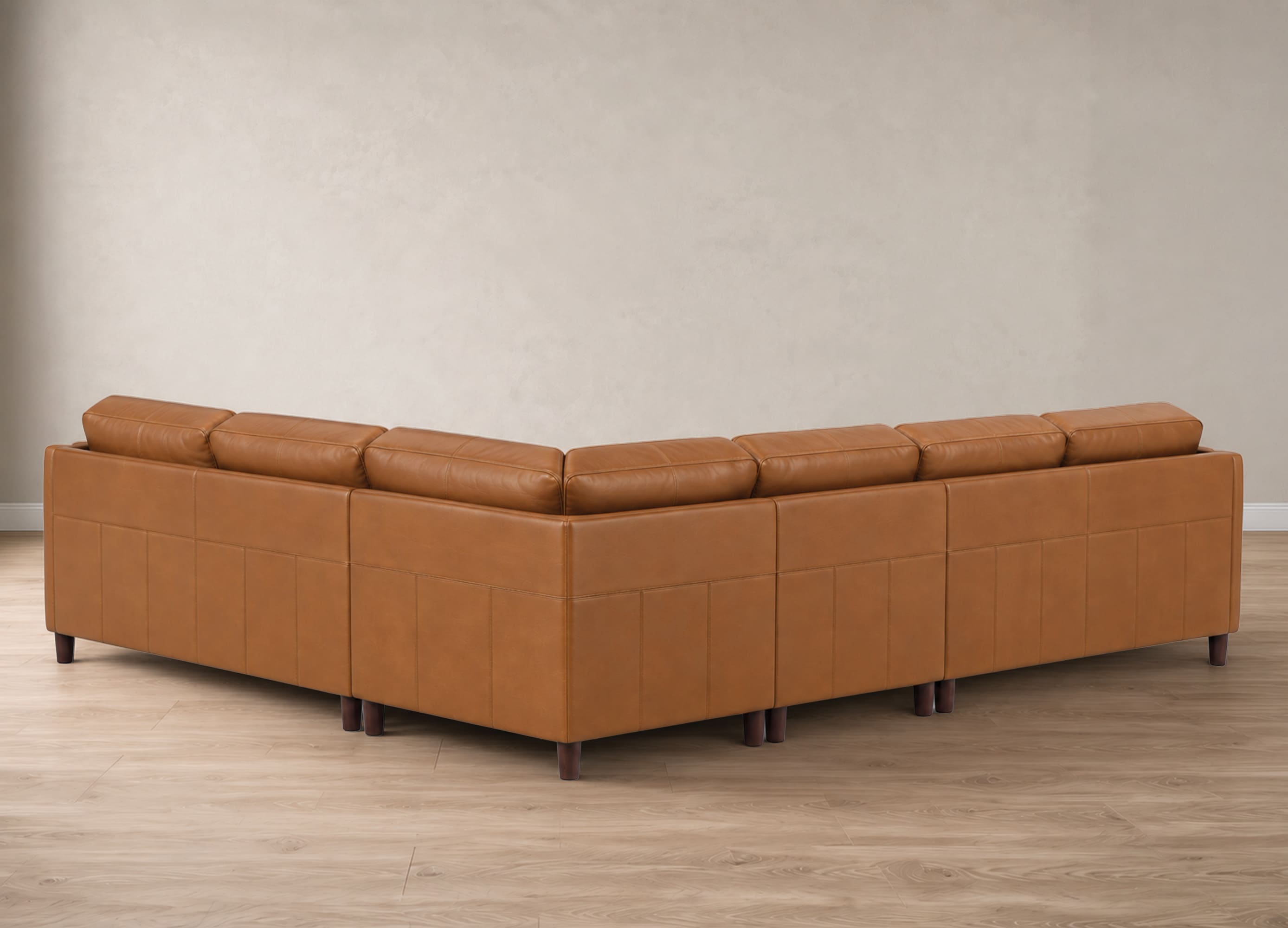 A modern sectional sofa upholstered in warm tan leather, shown from a three-quarters angle in a minimalist room with a textured beige wall and light wood flooring.