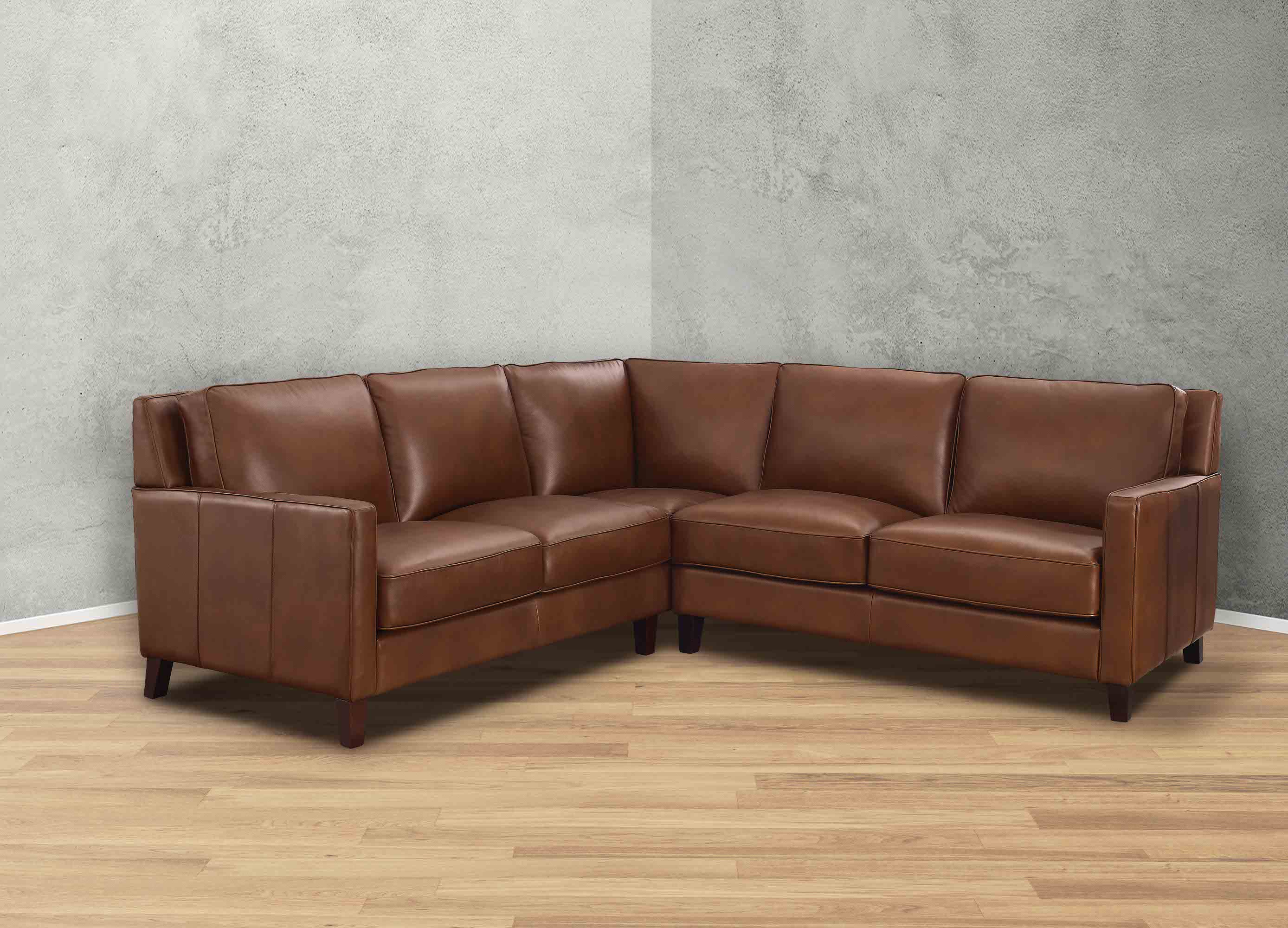 Brown leather sectional sofa in a room with gray walls and wooden flooring.