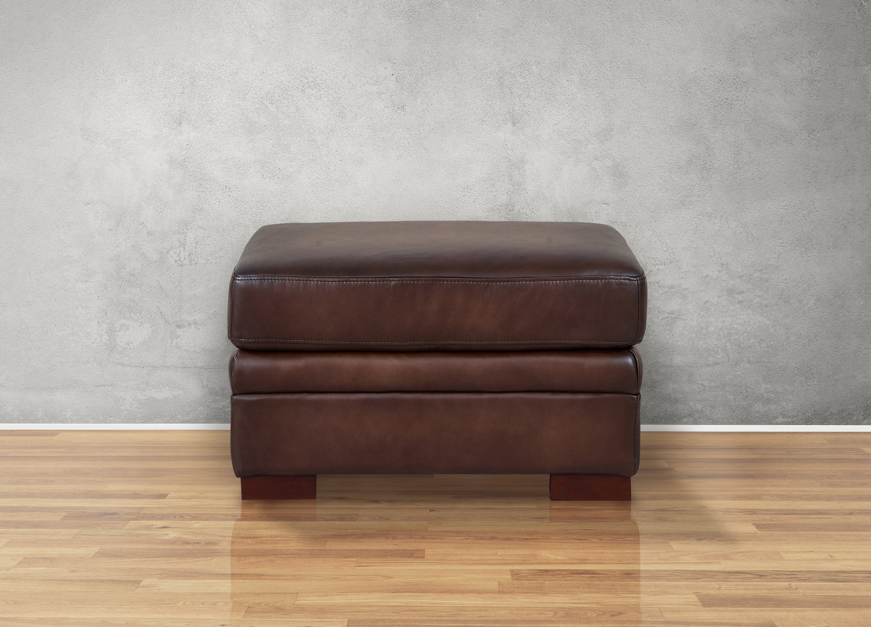 Brown leather ottoman on a wooden floor with a gray textured wall background