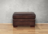 Brown leather ottoman on a wooden floor with a gray textured wall background