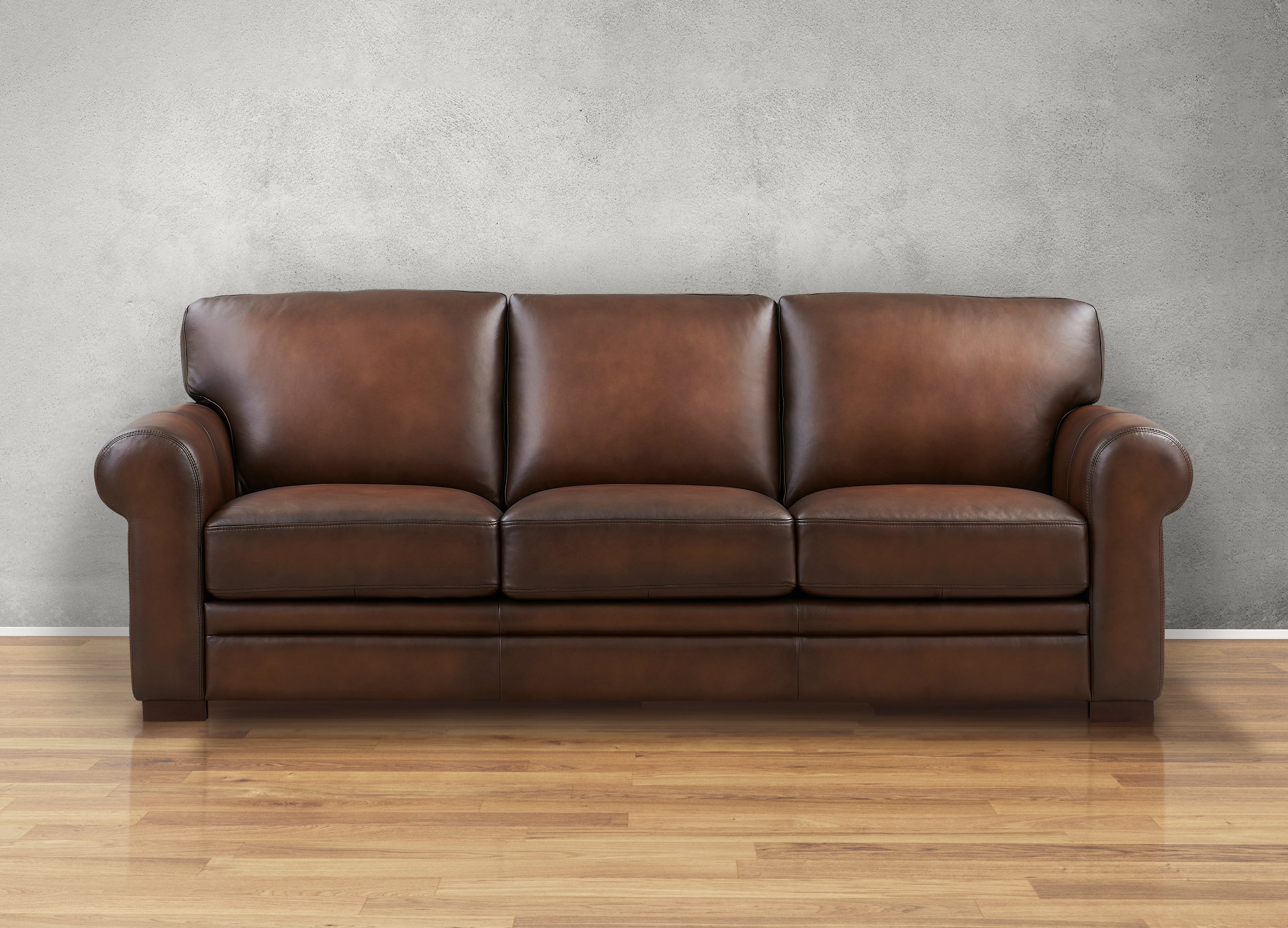 Brown leather sofa on a wooden floor with a gray wall background