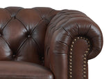 Close-up of a brown leather armchair with tufted backrest and nailhead trim.