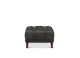 A black tufted ottoman with dark brown wooden legs, shown from the front against a plain white background.