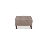 A square tufted ottoman in taupe-brown faux leather with dark brown wooden legs, shown against a plain white background.
