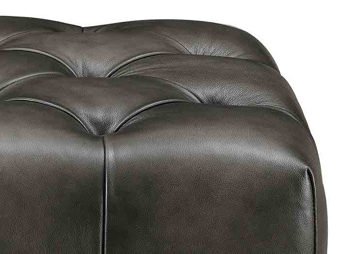 Close-up of a dark gray leather ottoman with tufted design on a white background