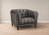 A dark gray tufted leather armchair with dark wooden legs, positioned on a light wood floor against a neutral beige wall.