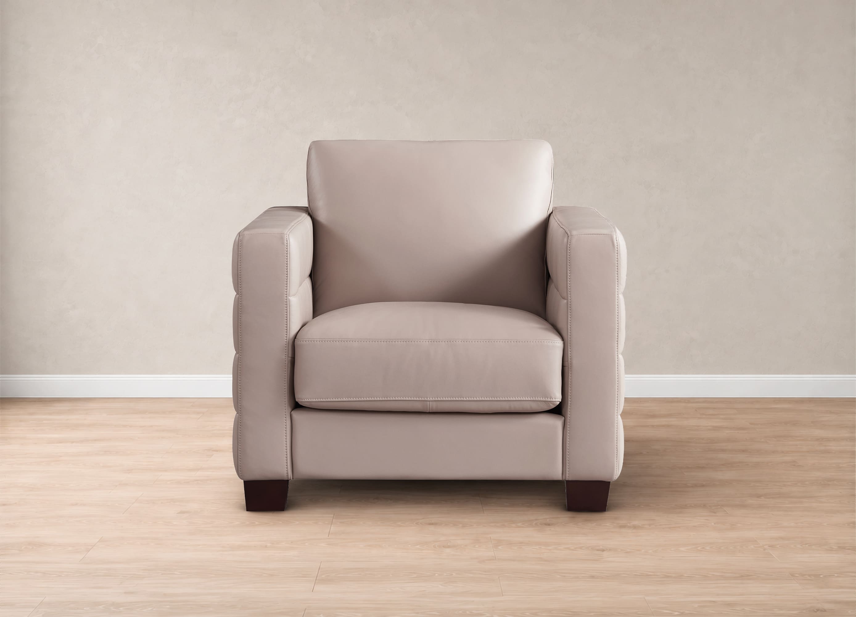 A single upholstered armchair in a light beige or taupe leather-like material, shown centered against a neutral beige wall and light wood floor.