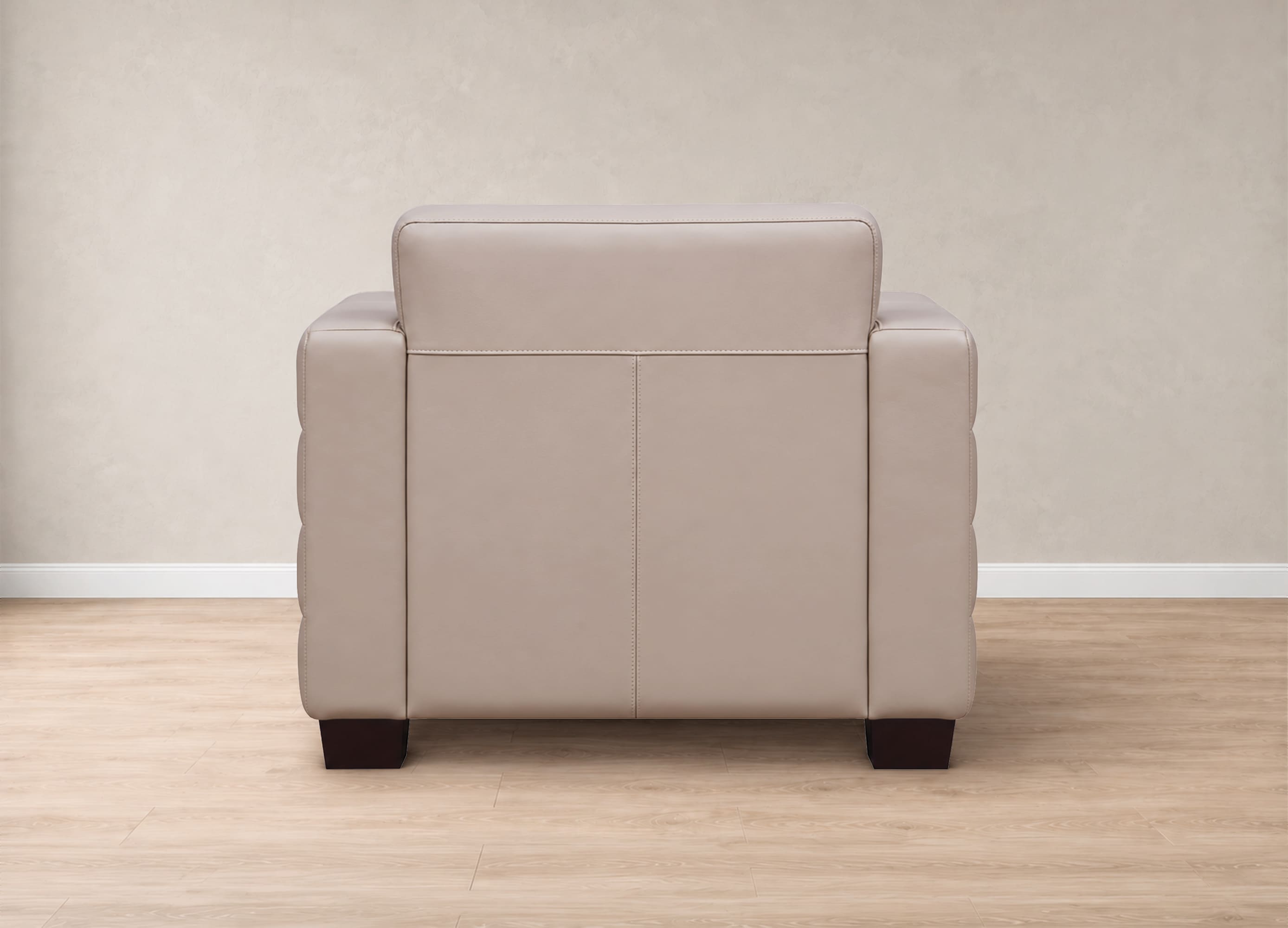 A light beige leather armchair shown from the back, positioned on a light wood floor against a neutral beige wall.