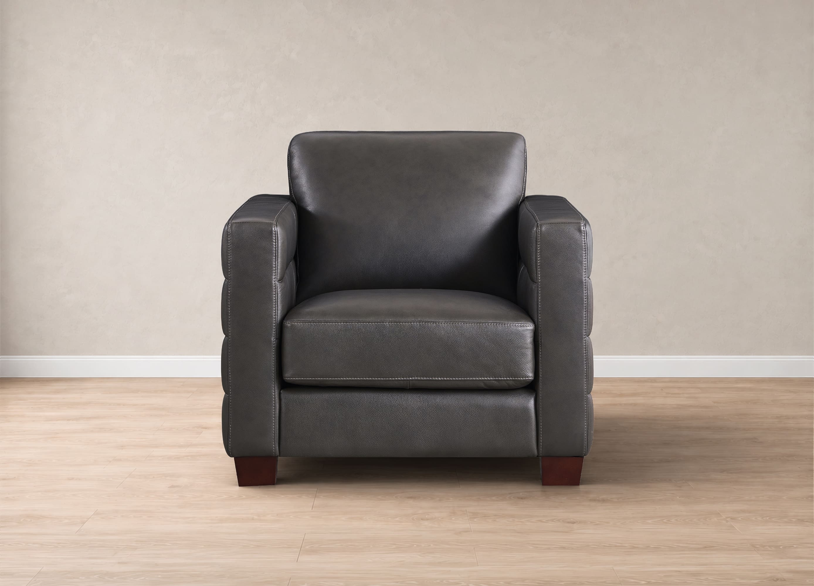 A dark gray leather armchair with square arms and a high back, set against a neutral beige wall and light wood floor.