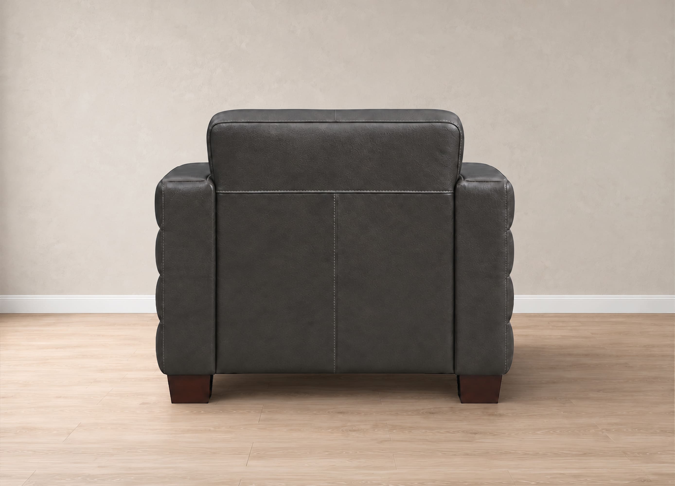 A dark gray faux leather armchair with chunky, scalloped armrests and dark wooden legs, shown from the back against a neutral beige wall and light wood floor.