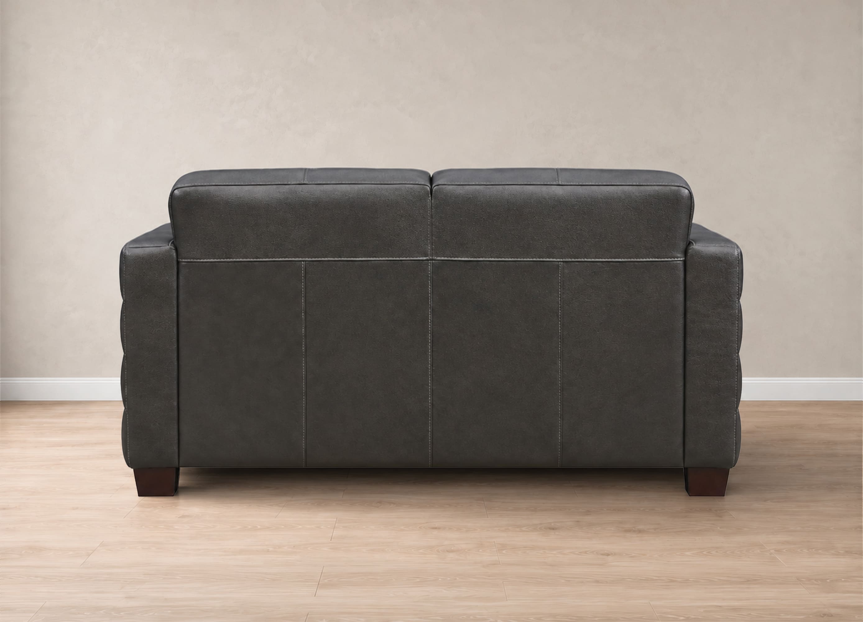 A dark gray upholstered loveseat shown from the back, positioned on a light wood floor against a textured beige wall.