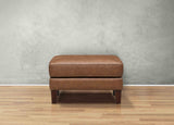 Brown leather ottoman on a wooden floor with a gray wall background