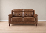 A brown leather loveseat with tufted back cushions and dark wooden legs, set against a neutral beige wall and light wood floor.