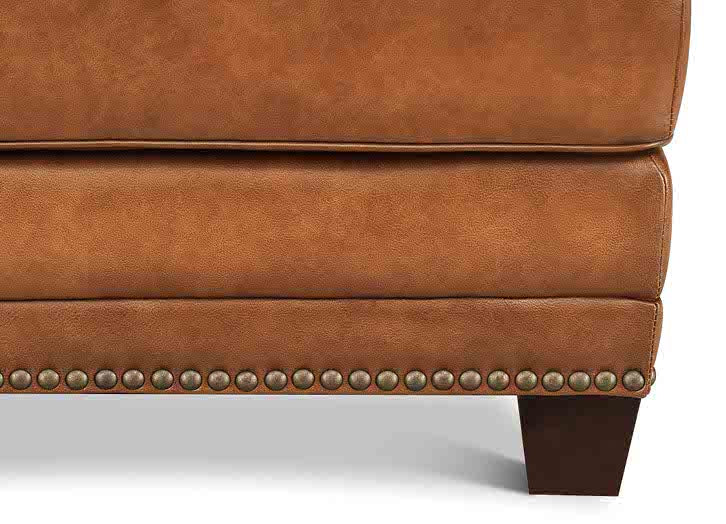 Close-up of a brown leather armchair with studded details on a white background