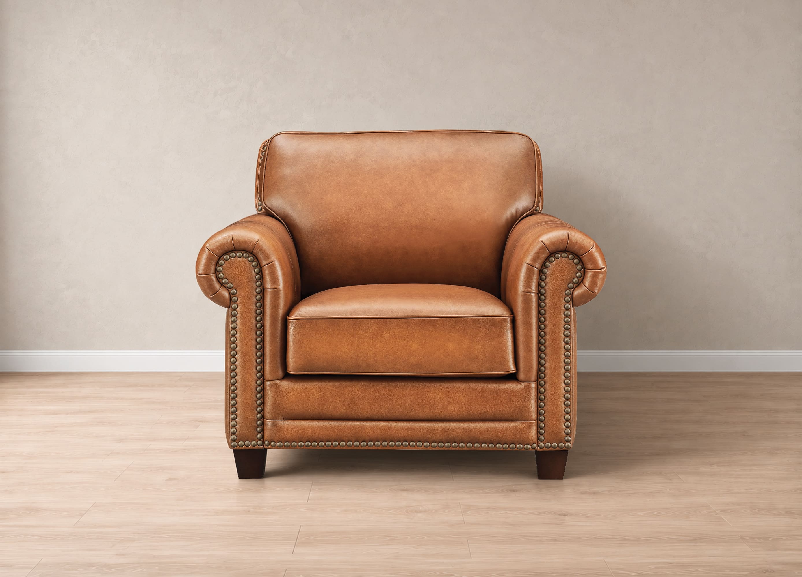 A classic brown leather armchair with rolled arms, nailhead trim, and dark wooden legs, set against a neutral beige wall and light wood floor.