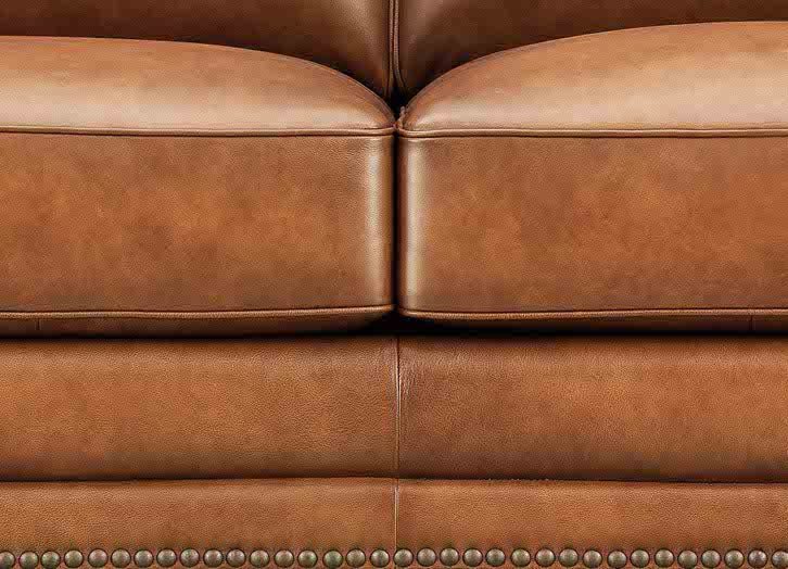 Close-up of a brown leather sofa with visible stitching and nailhead trim.