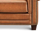 Close-up of a brown leather sofa with nailhead trim on a white background