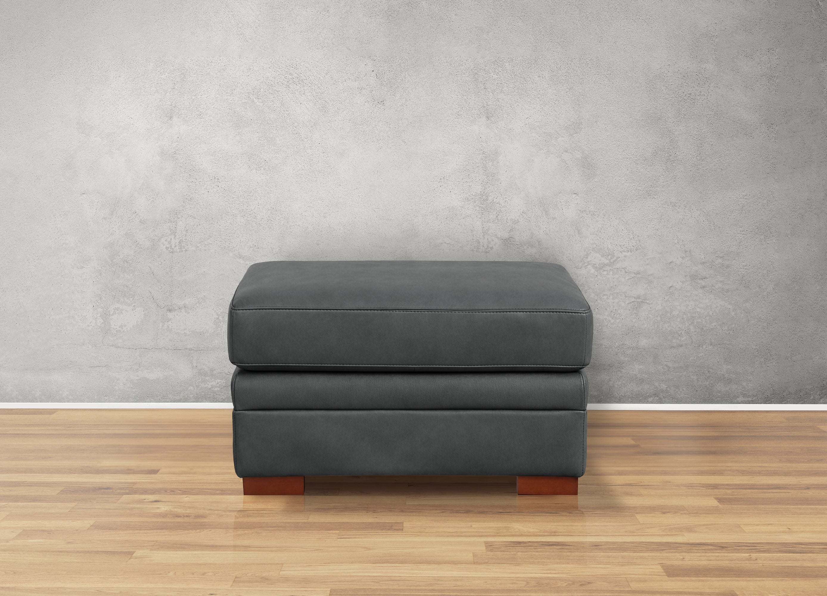 Gray ottoman with wooden legs on a wooden floor against a gray wall