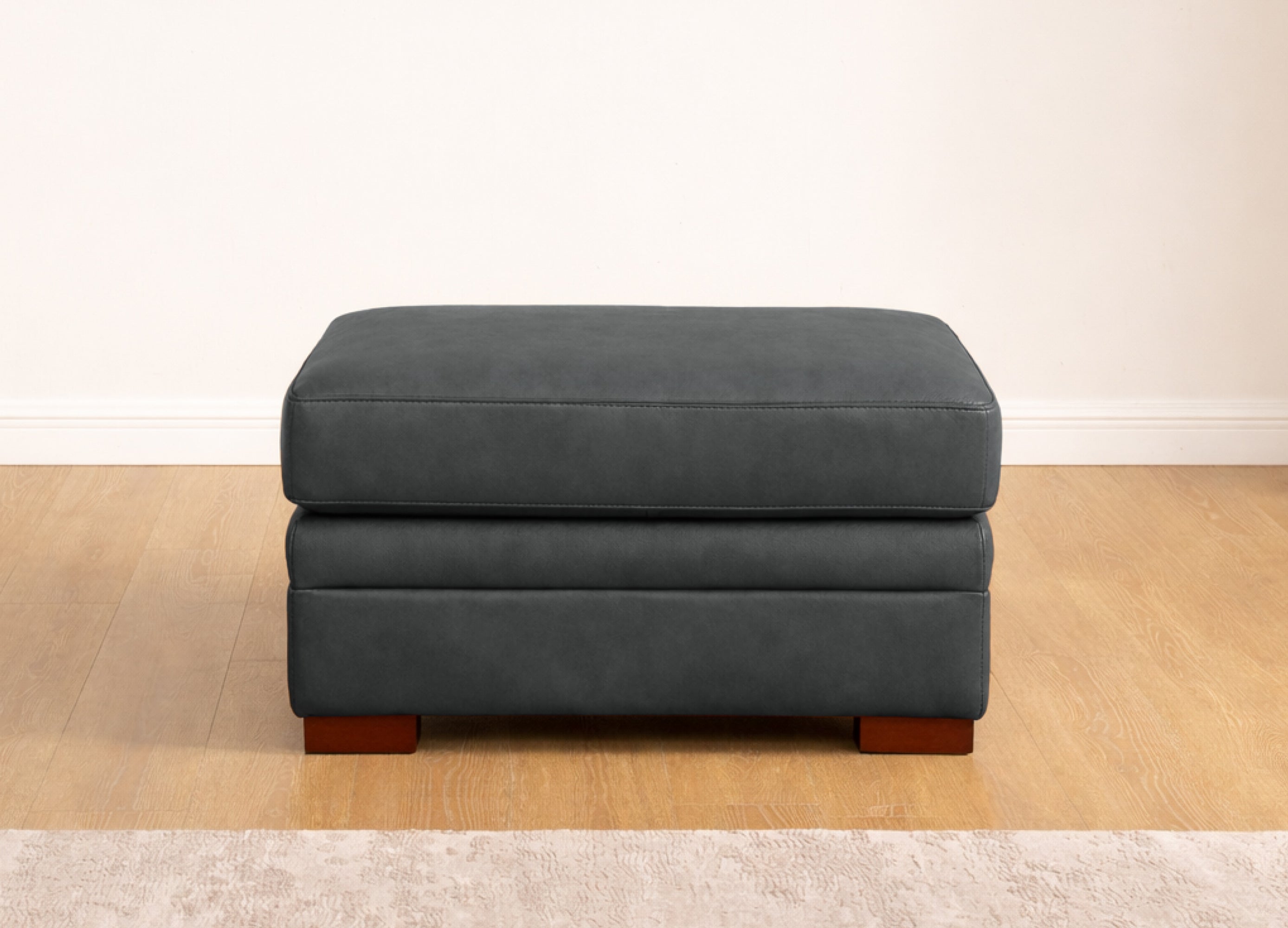 Gray ottoman on a wooden floor with a white wall background