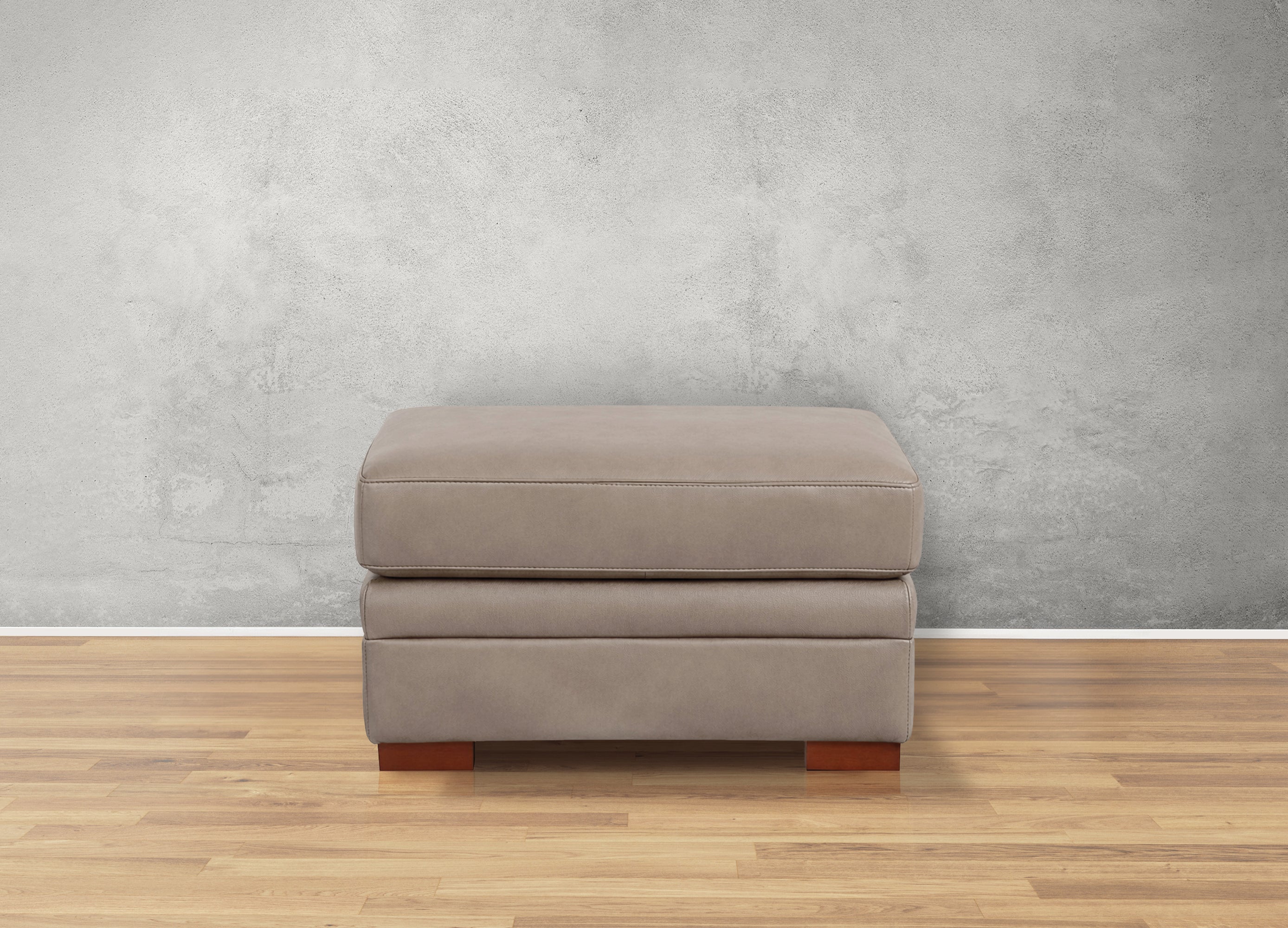 Gray ottoman with wooden legs on a wooden floor against a gray wall