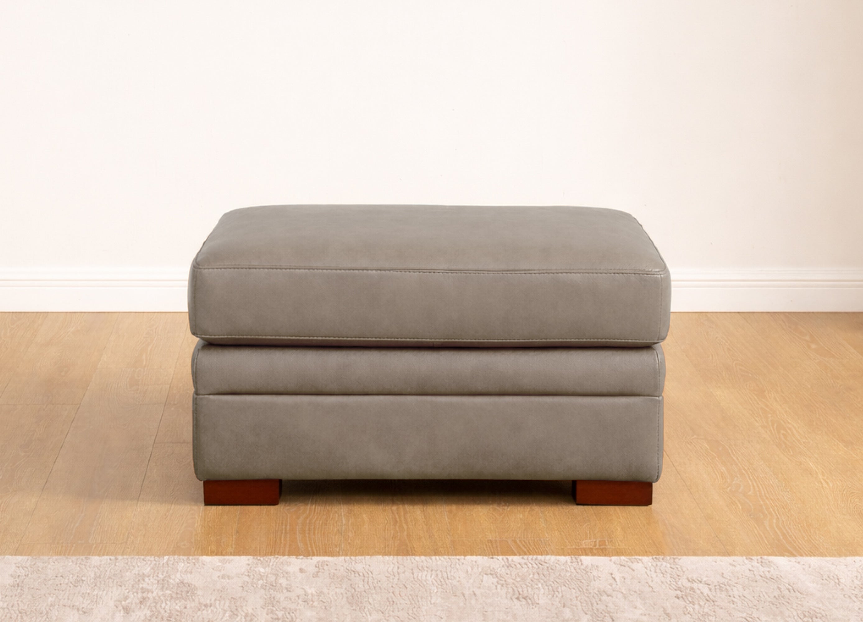 Gray ottoman on a wooden floor with a white wall background