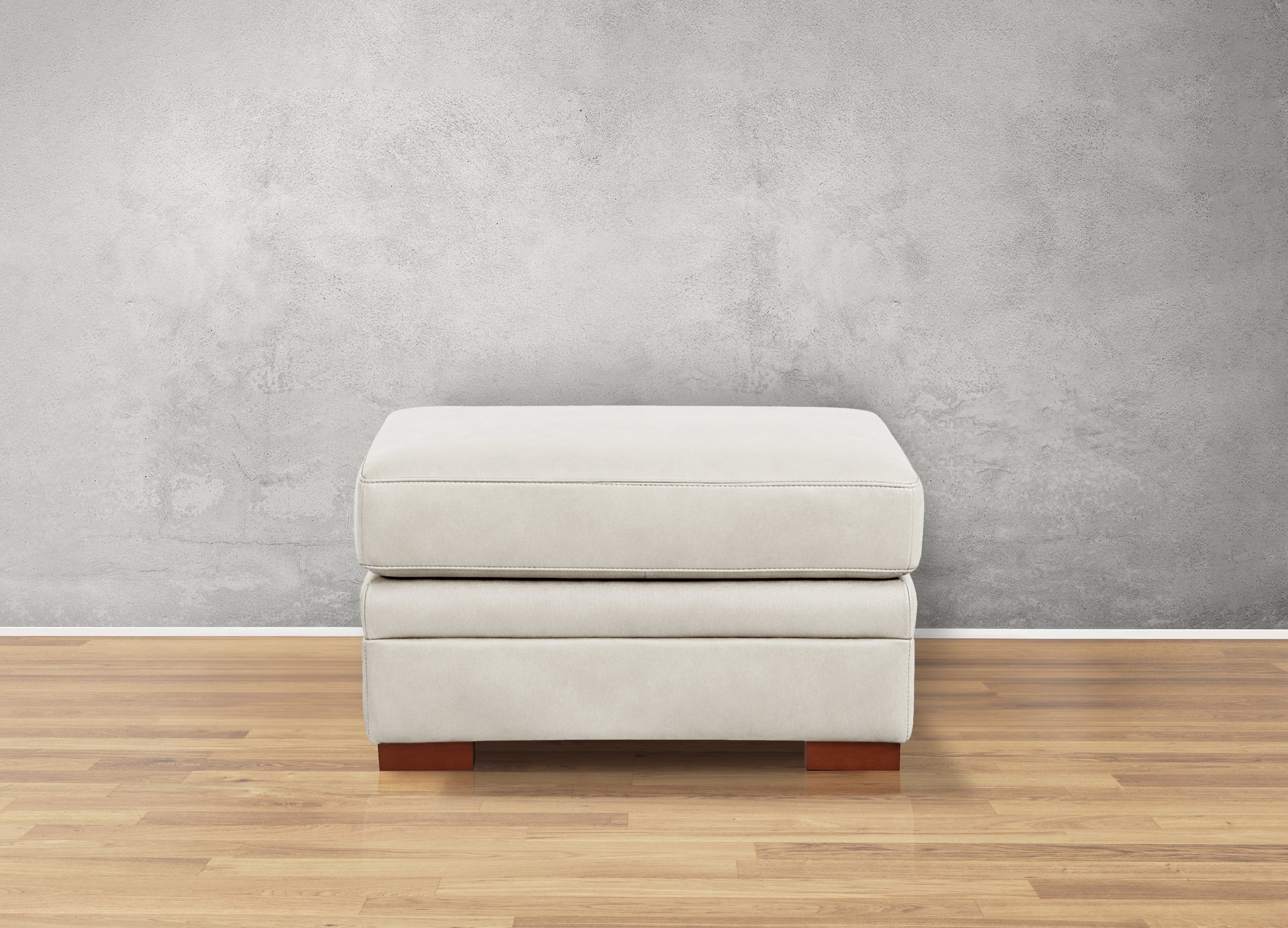 White ottoman with wooden legs on a wooden floor against a gray wall