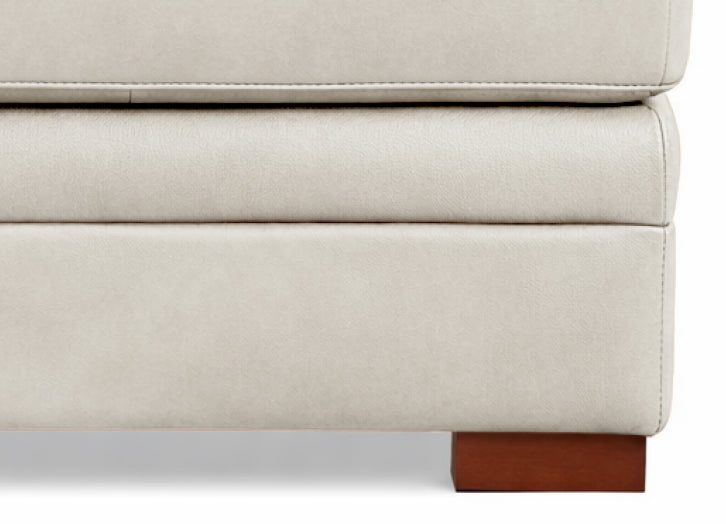 Close-up of a beige upholstered piece of furniture with wooden legs on a white background