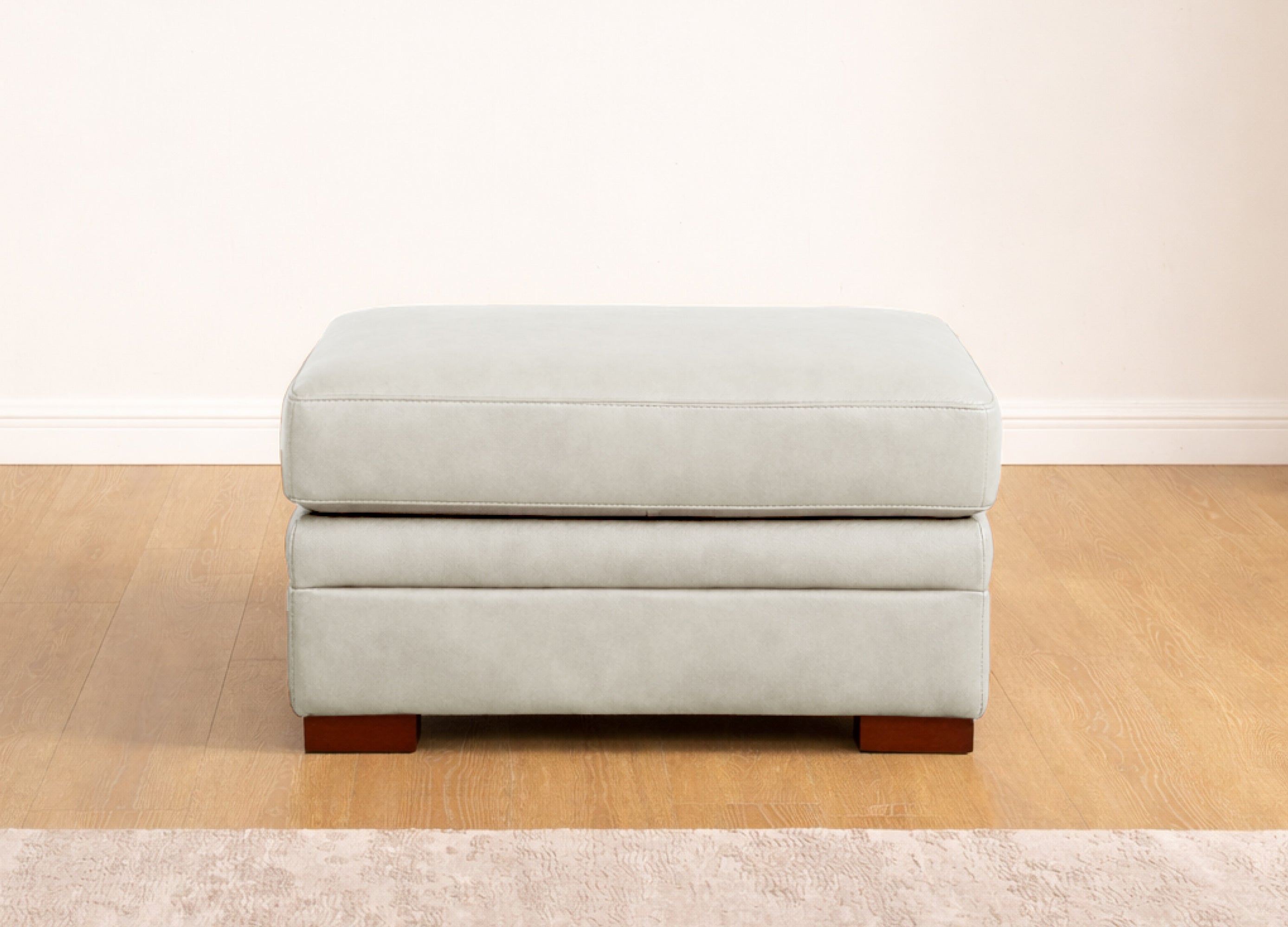 Light gray ottoman with wooden legs on a beige floor.
