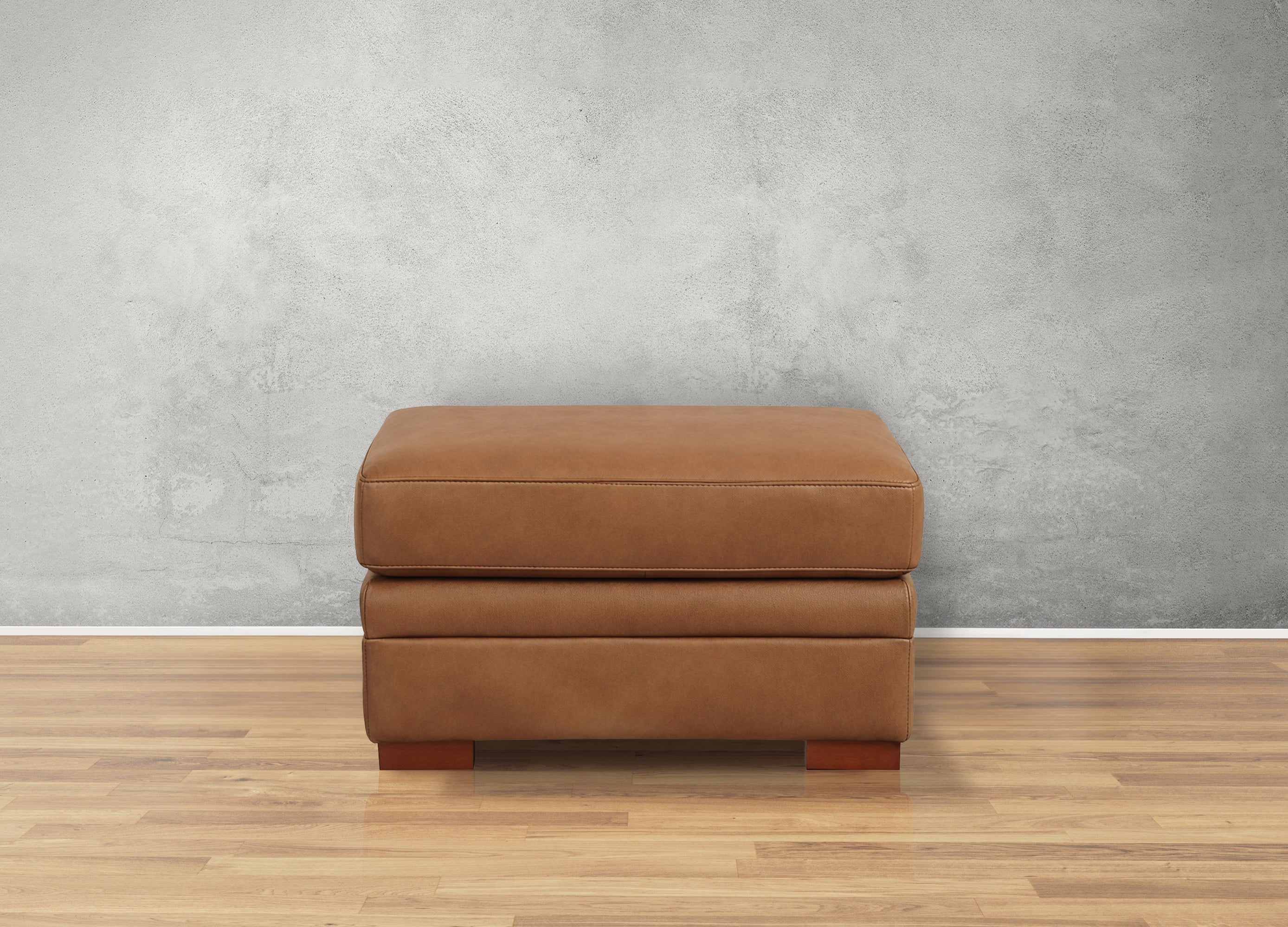 Brown leather ottoman on a wooden floor with a gray wall background