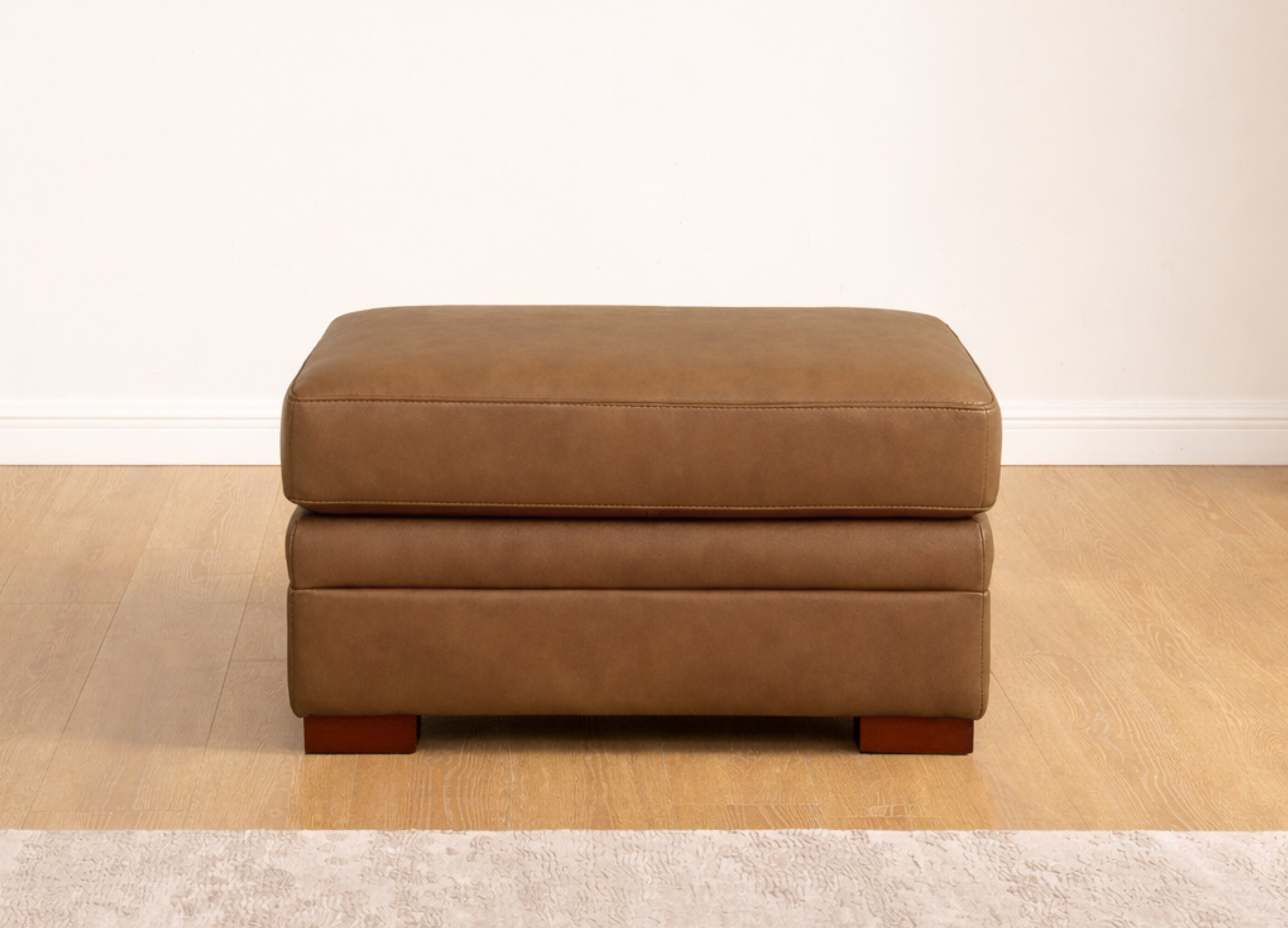 Brown ottoman on a wooden floor with a white wall background