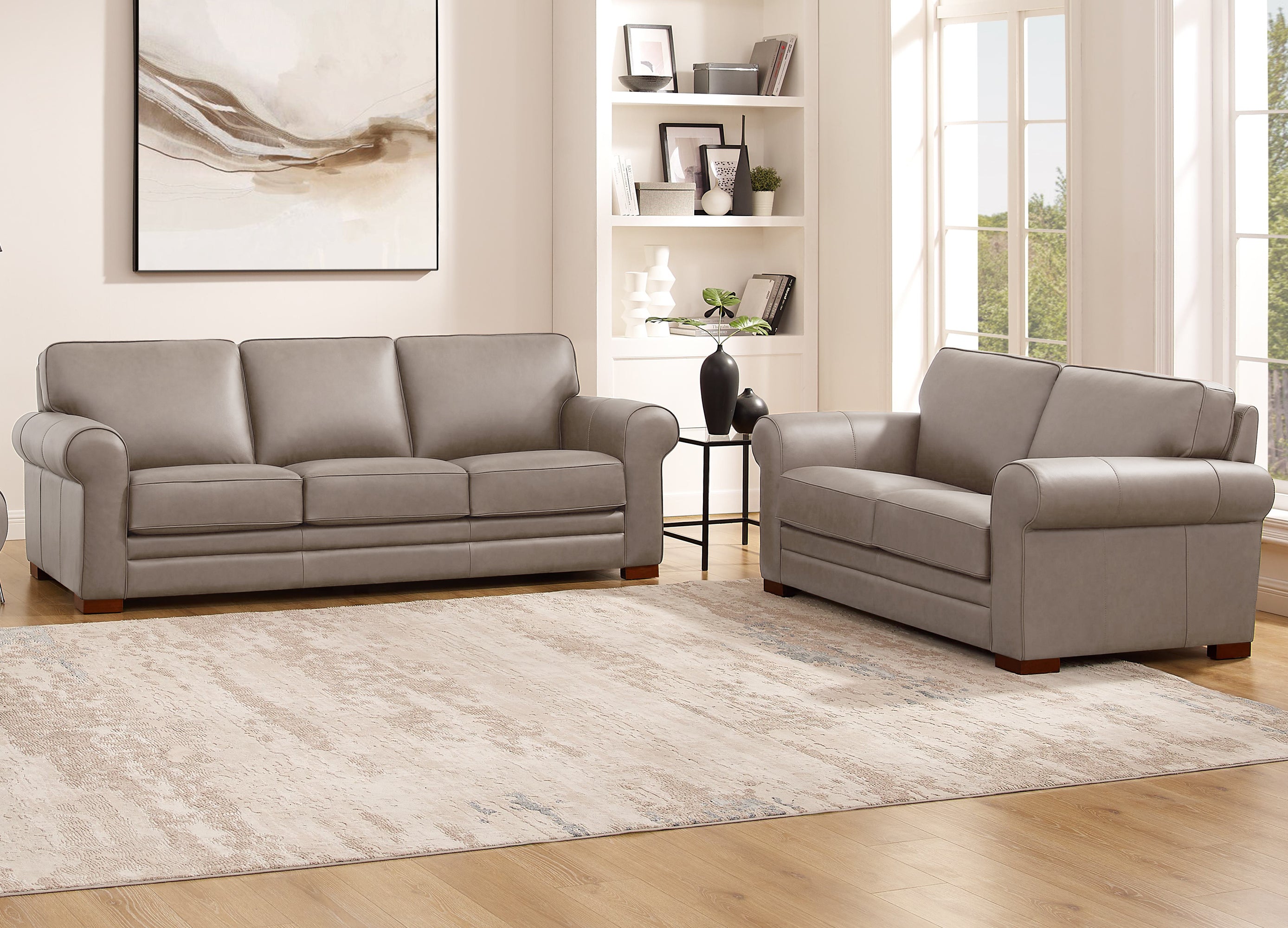 Gray leather sofa set in a living room with a rug and bookshelf.