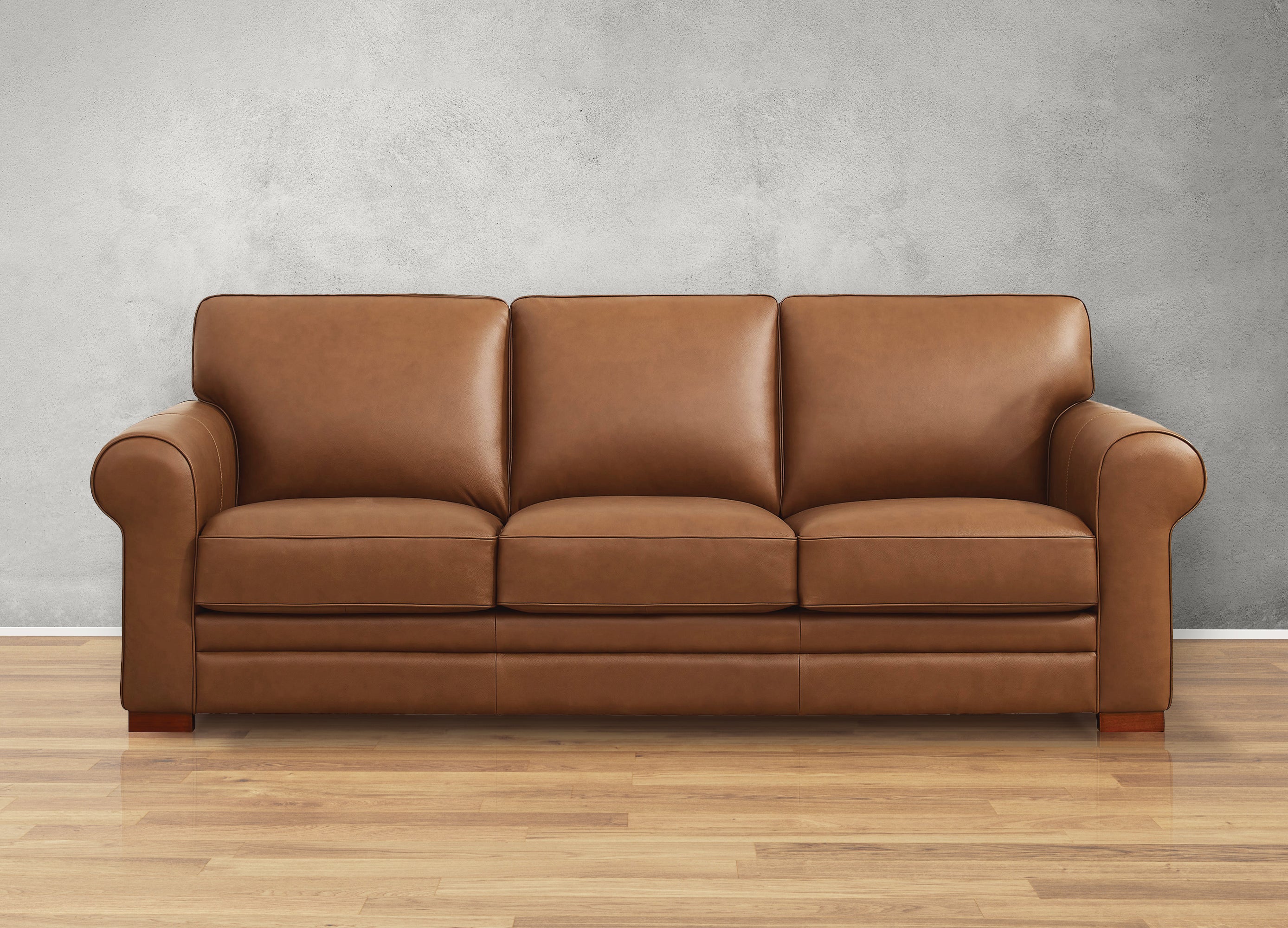Brown leather sofa on a wooden floor with a gray wall background