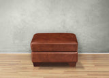 Brown leather ottoman on a wooden floor with a gray wall background
