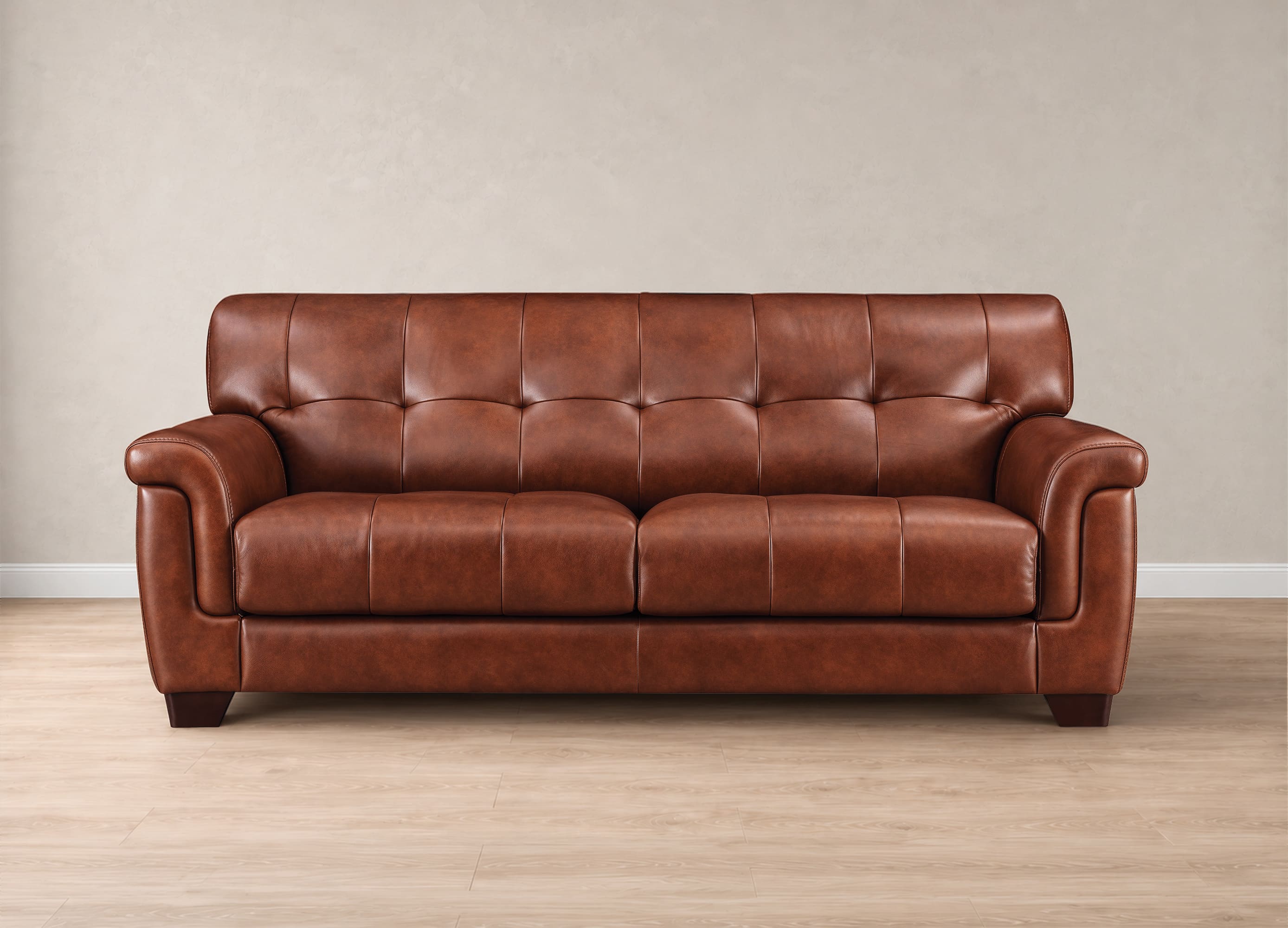 A brown leather sofa Marylynn with a tufted backrest and rolled arms, shown against a neutral beige wall and light wood floor.