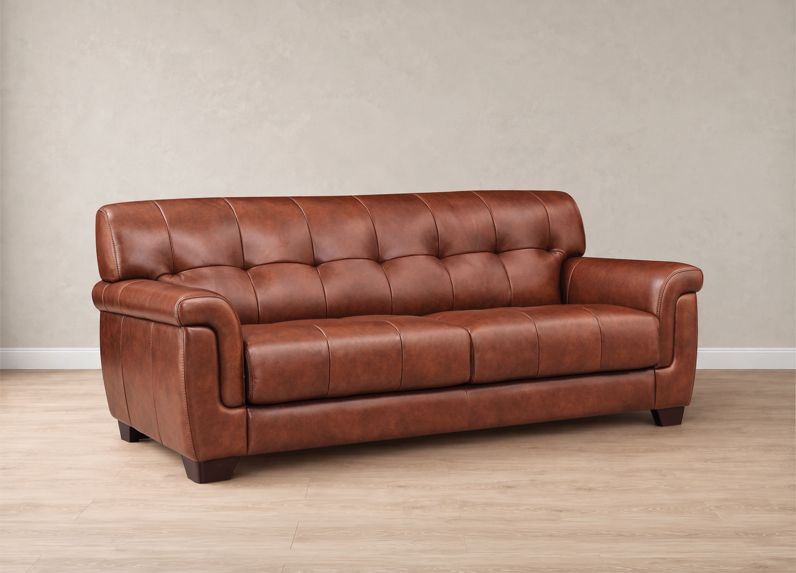 A brown leather sofa Marylynn with tufted button details on the backrest and seat, shown in a studio setting with a textured beige wall and light wood floor.