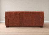 A brown leather sofa with vertical channel tufting and rolled arms, shown from the back against a neutral beige wall and light wood floor.