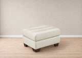 A square ottoman upholstered in light cream leather with tufted stitching on the top cushion and dark brown wooden legs, shown in a minimalist room setting with a beige wall and light wood floor.