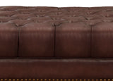 Brown leather sofa with tufted backrest and nailhead trim on a white background
