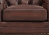 Close-up of a brown leather armchair with tufted backrest and nailhead trim.