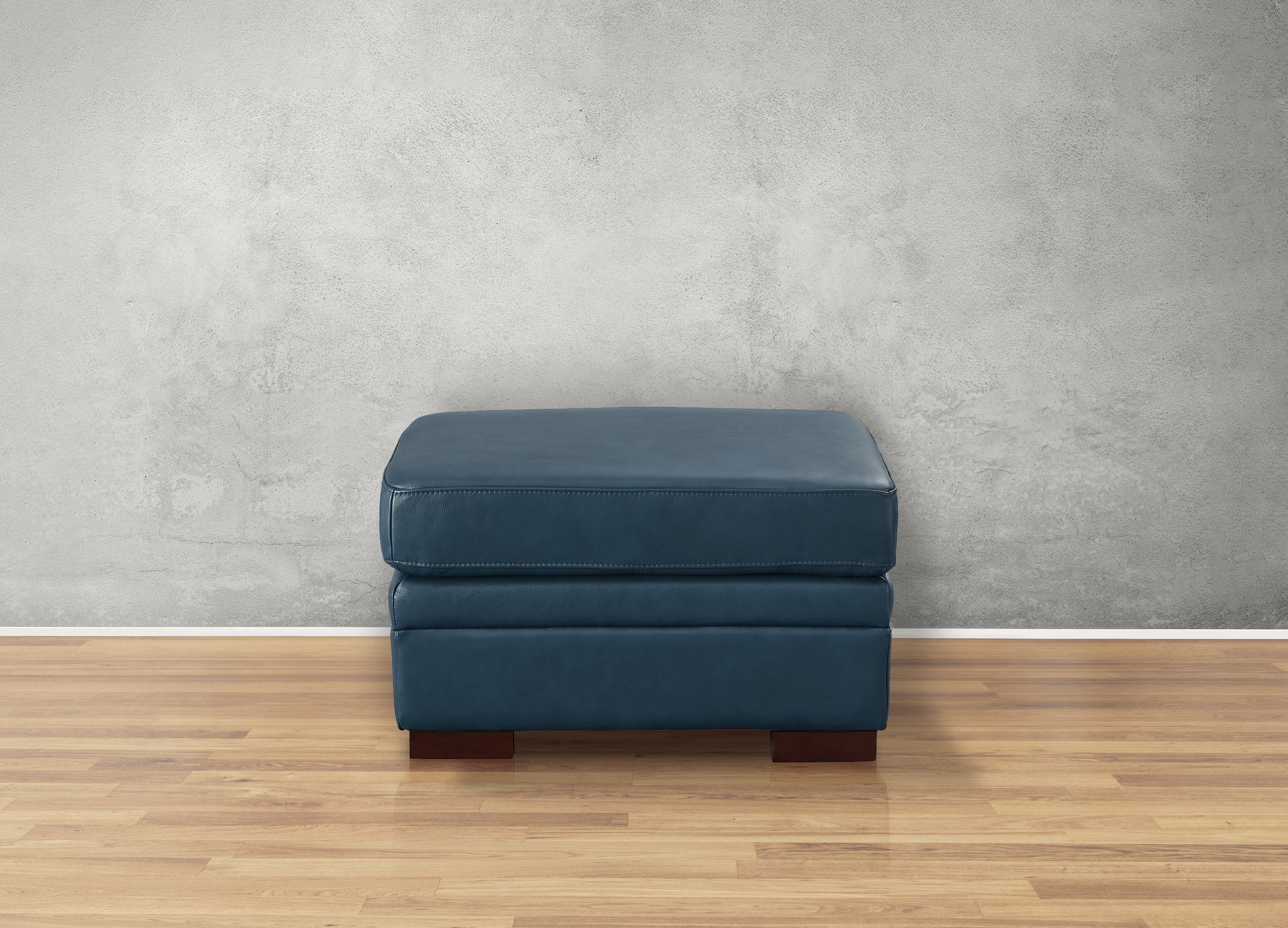 Blue ottoman on a wooden floor with a gray wall background