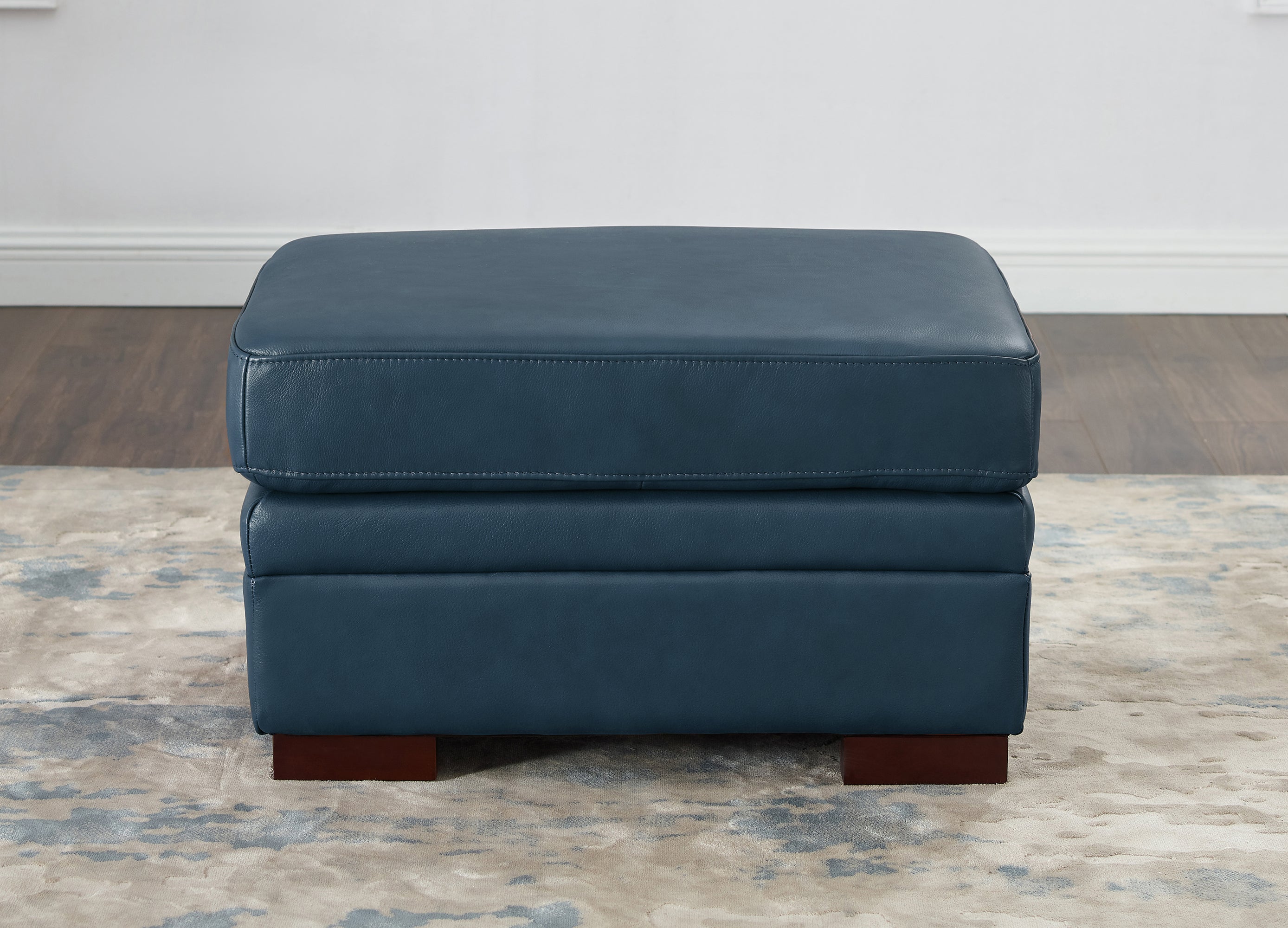 Blue ottoman on a patterned rug with a neutral wall background