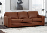 Brown leather sofa in a living room with large windows and abstract art on the wall.